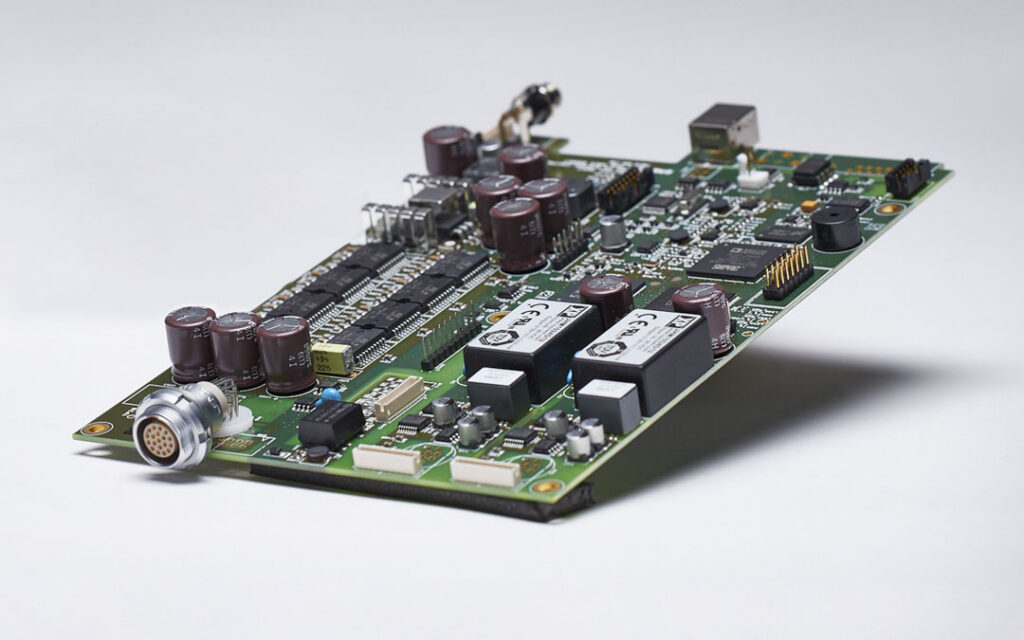 Aurora System Control Unit printed circuit board assembly showing capacitors, integrated circuits, transformers, and a multi-pin connector along the edge.