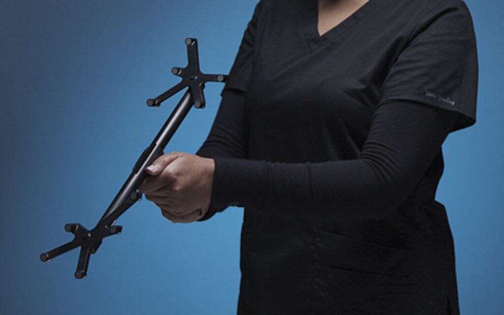 Person in black scrubs holding a Polaris Accuracy Assessment Kit with two four-marker rigid body tool arrays mounted on a black shaft.