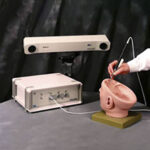 The Aurora electromagnetic tracking system with its field generator positioned above a head-shaped phantom, with a tracked instrument inserted into the model. Released in 2001.