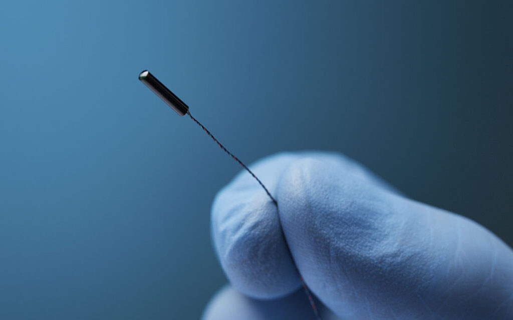 Close-up of a gloved hand holding an Aurora electromagnetic sensor coil by its thin lead wire.
