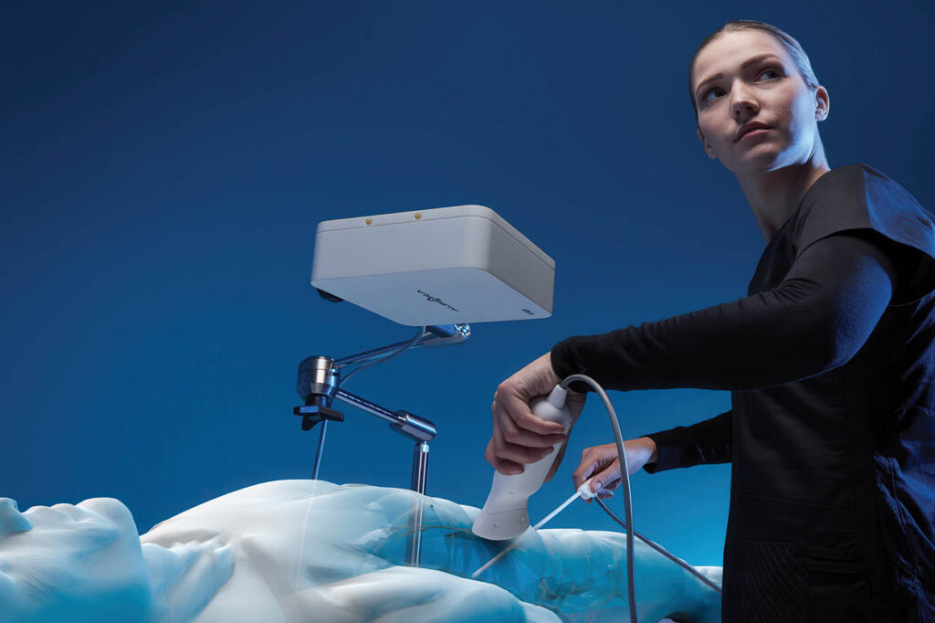 NDI Aurora electromagnetic tracking system, showing the field generator mounted on an articulated arm above a patient while a person holds a tracked sensor tool.