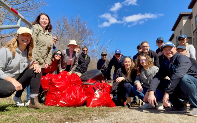 Group of NDI employees gathered outdoors on a sunny day, posing with collected red garbage bags during a community cleanup event.